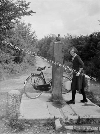 WOMAN WITH BIKE AT VILLAGE PUMP